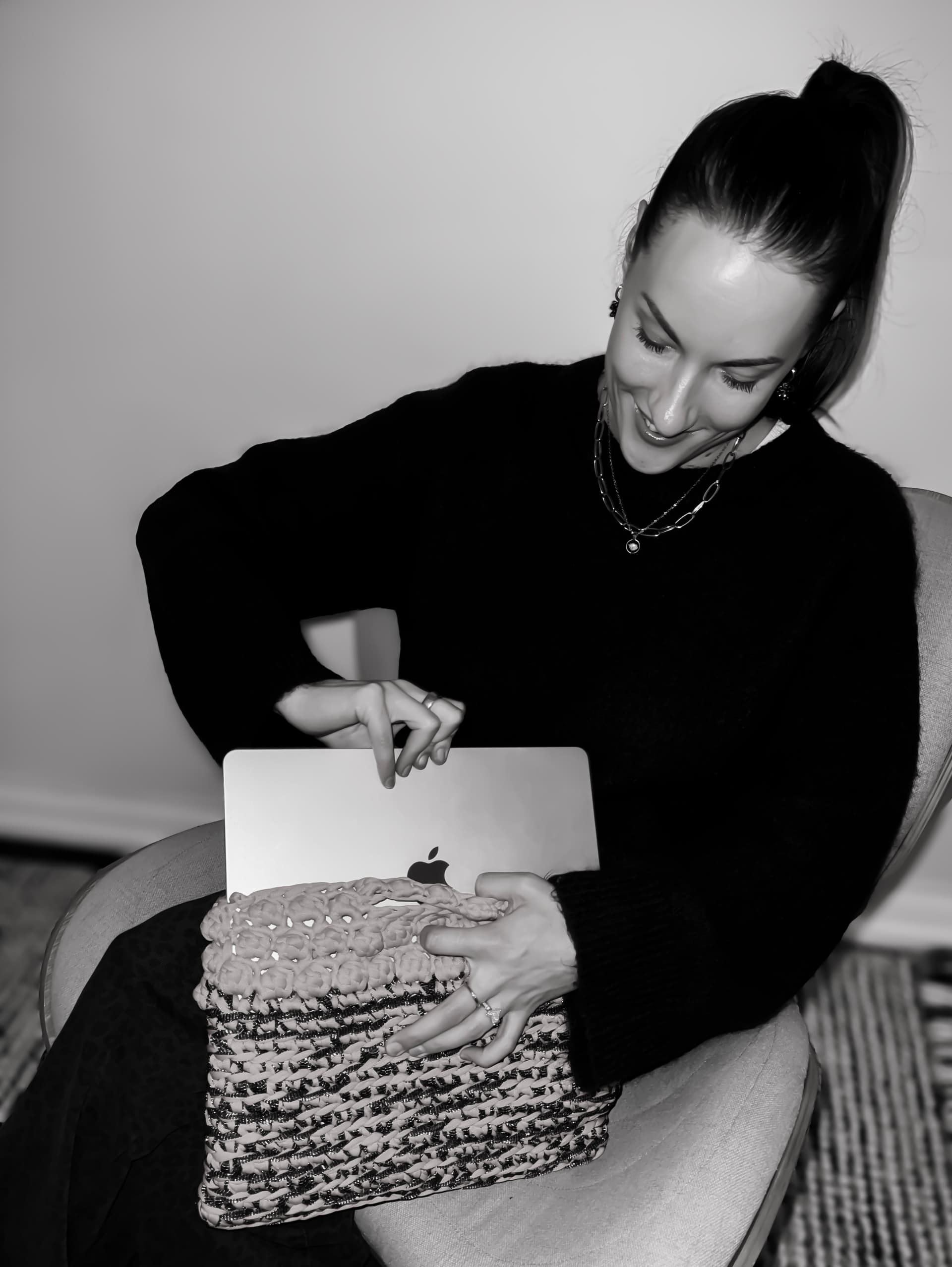 A sister with a handmade crochet bag on her lap and a laptop tucked inside it.