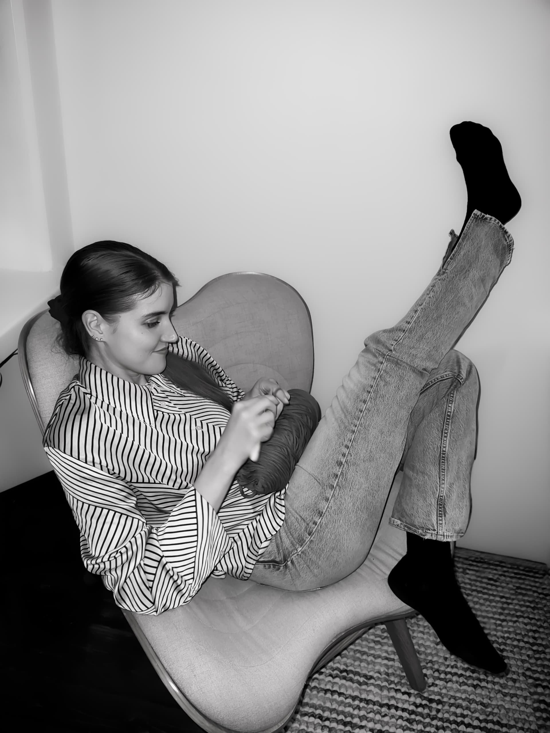 One of the sisters crocheting in an armchair, feet up.