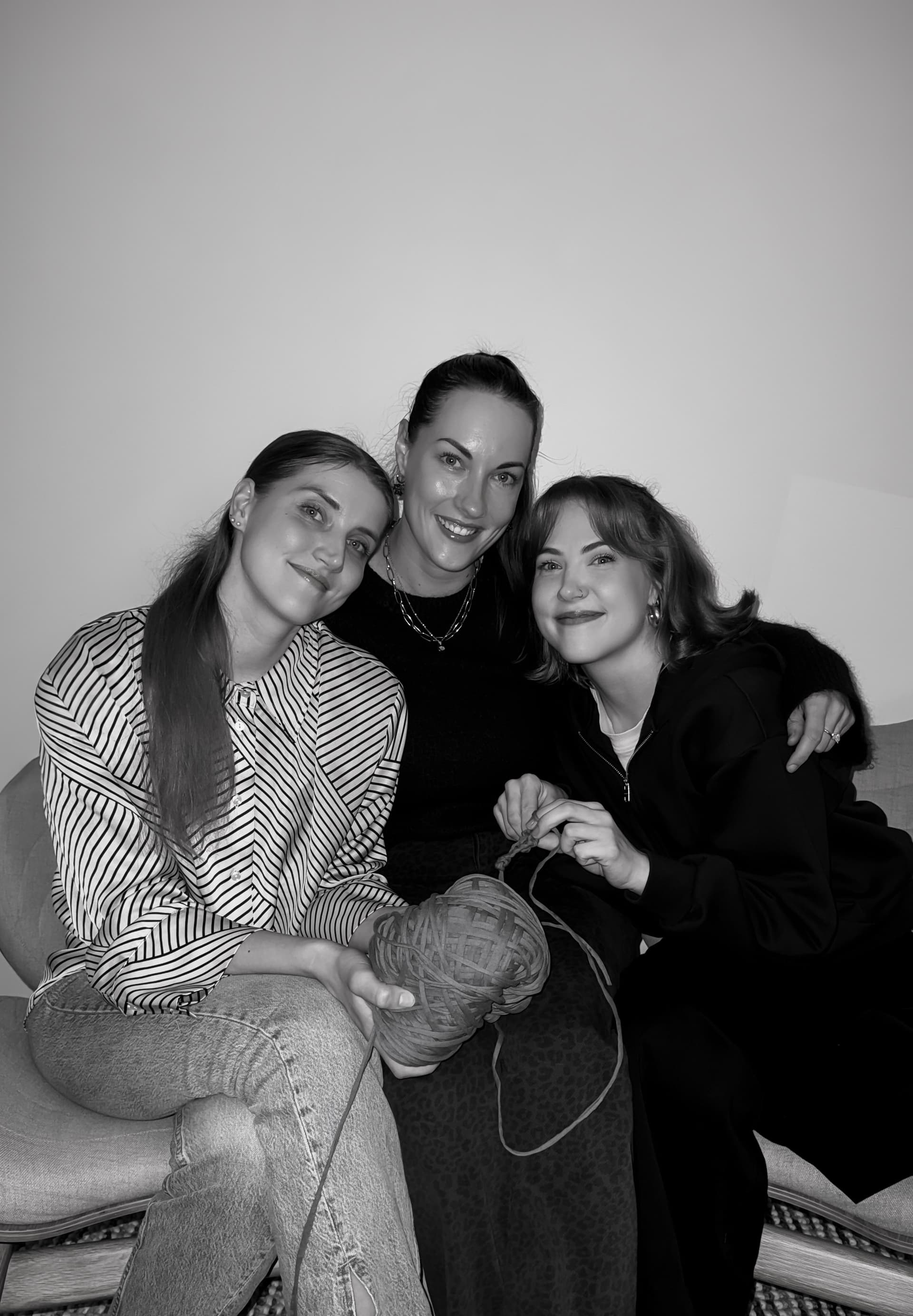 Three sisters sitting together, one holding a ball of yarn.